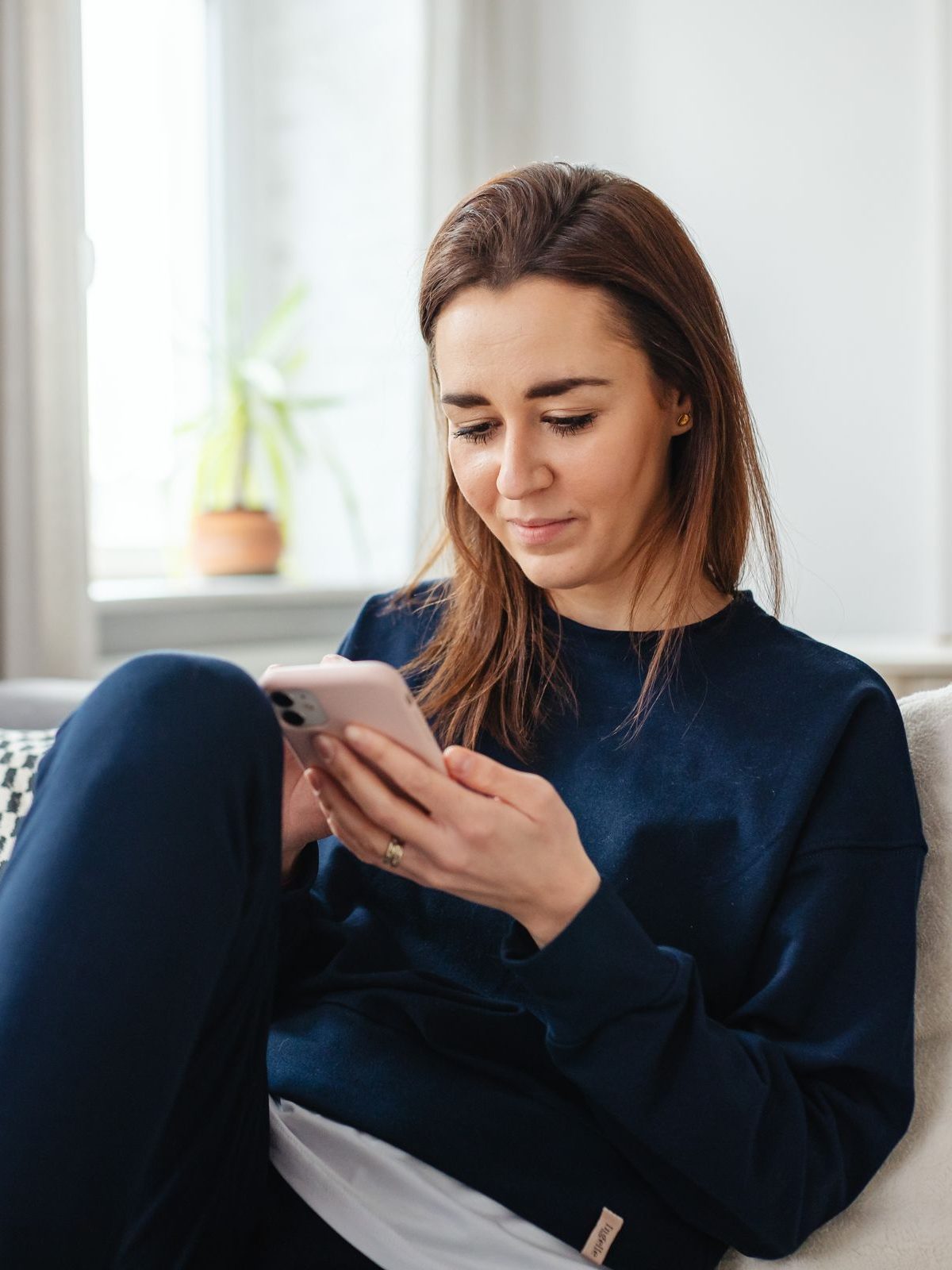 A woman sitting on her sofa at home, checking her phone.