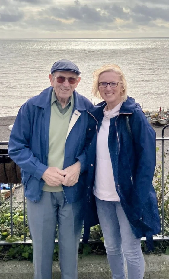 Maddy and her dad John standing together by the sea.
